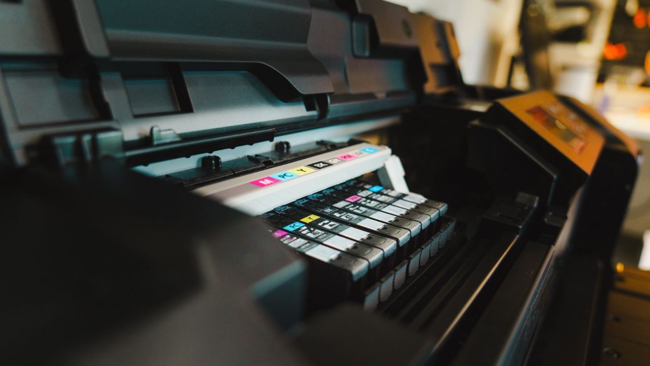 Close-up view of a printer with multiple colored ink cartridges visible in the cartridge compartment, showing cyan, magenta, yellow, and black ink cartridges ready for printing.
